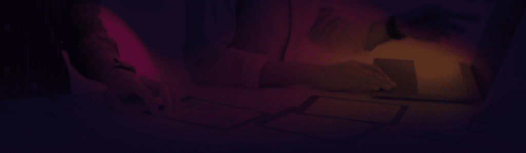 Gradient overlay on top of the hands of two people working on a laptop and paper with mobile wireframe designs.