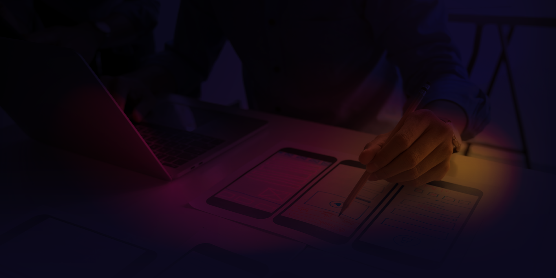 Gradient overlay on top of a man sitting in front of a laptop and paper working on mobile wireframe designs.